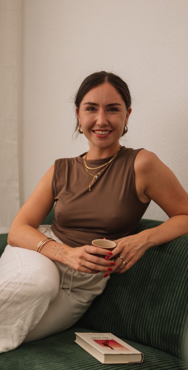 Giorgia Nebuloni Heilpraktikerin für Psychotherapie Das Bild zeigt Giorgia Nebuloni, eine Heilpraktikerin für Psychotherapie aus Köln, vor einem Holzzaun, der von üppigem, grünem Laub und Pflanzen umgeben ist. Sie trägt ein schwarzes Kleid und lächelt sanft. Giorgia hat lange, dunkle Haare und trägt goldene Ohrringe. Die natürliche und beruhigende Umgebung reflektiert ihre einfühlsame und harmonische Herangehensweise in der Psychotherapie.